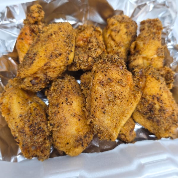 Close-up of golden-brown fried chicken wings seasoned with pepper, served in a foil-lined container.