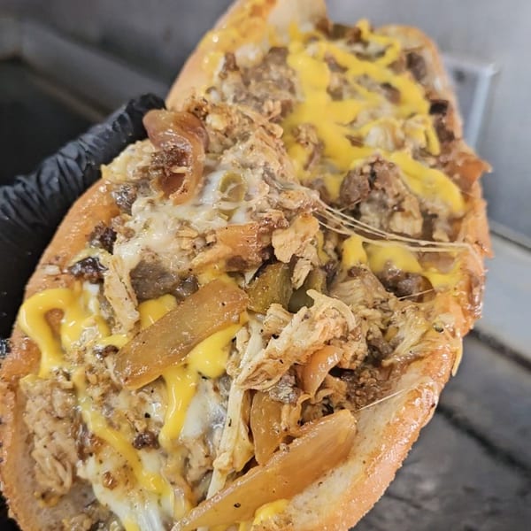 A close-up of a Tastee Buddies cheesesteak with melted cheese, steak, and onions.