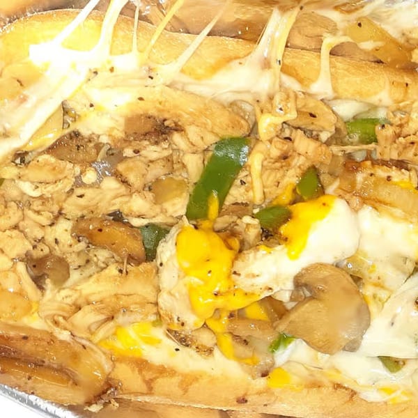 Close-up of a Tastee Buddies cheesesteak with chicken, melted cheese, green peppers, and mushrooms.