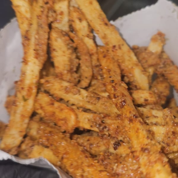Close-up of golden-brown seasoned fries in a white paper container from Tastee Buddies.