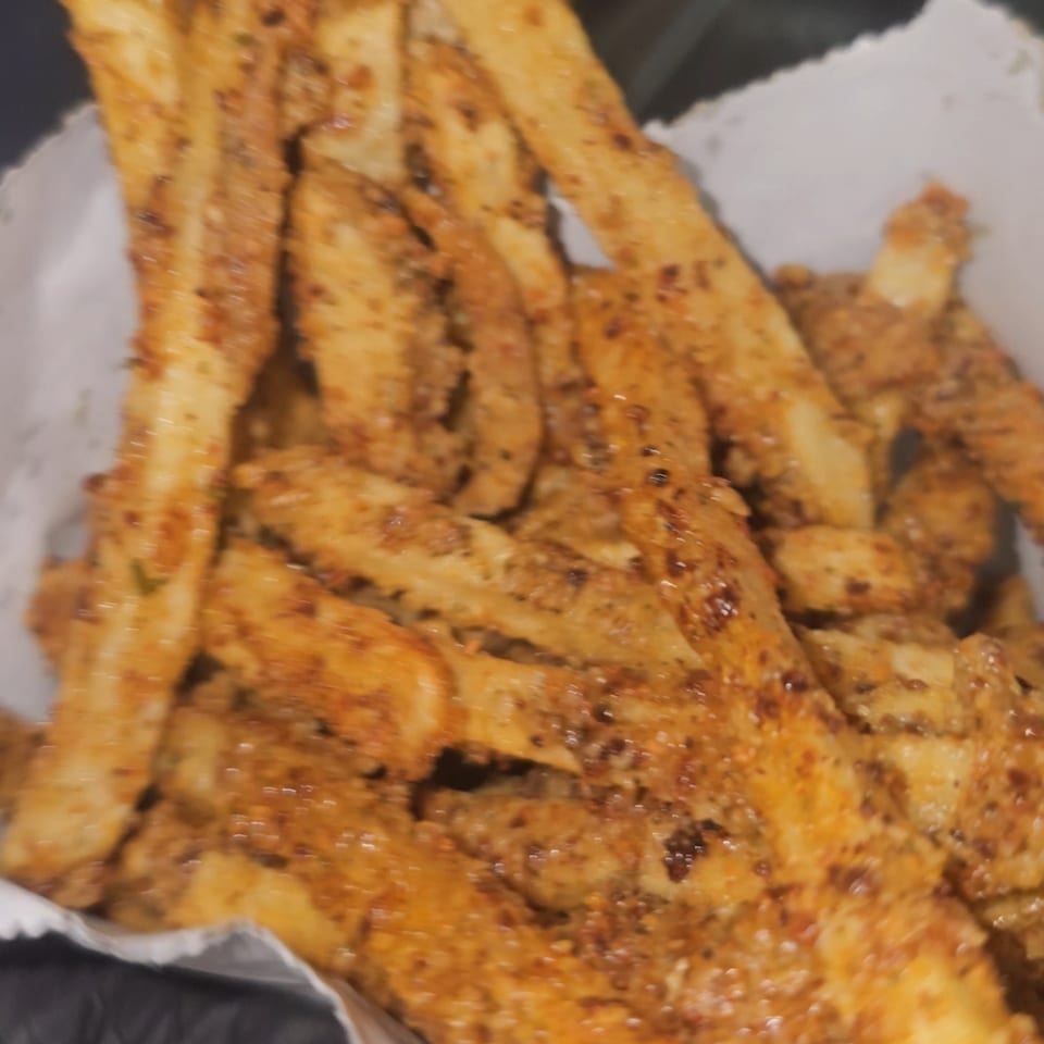 Close-up of golden-brown seasoned fries in a white paper container from Tastee Buddies.