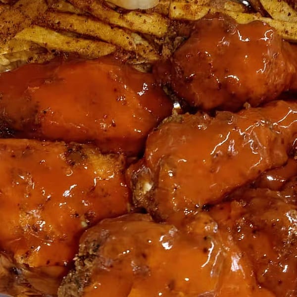 Close-up of Tastee Buddies' American-style chicken wings coated in a glossy orange sauce, with fries in the background.