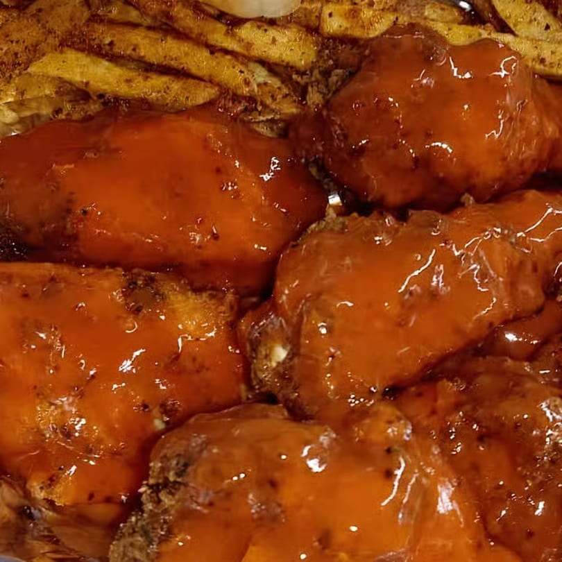 Close-up of Tastee Buddies' American-style chicken wings coated in a glossy orange sauce, with fries in the background.