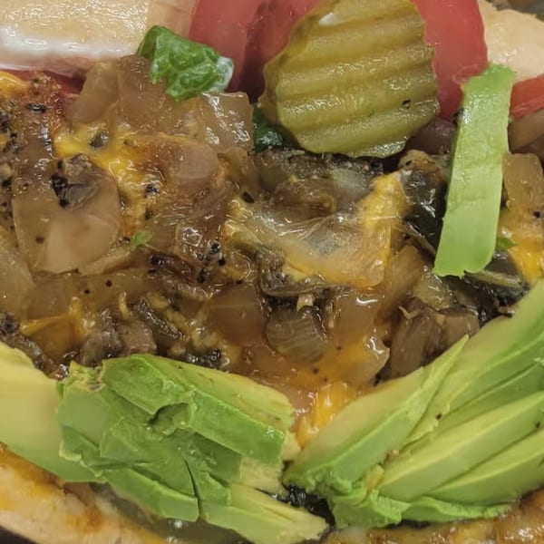 Close-up of a Tastee Buddies dish with melted cheese, caramelized onions, mushrooms, avocado, and pickles.
